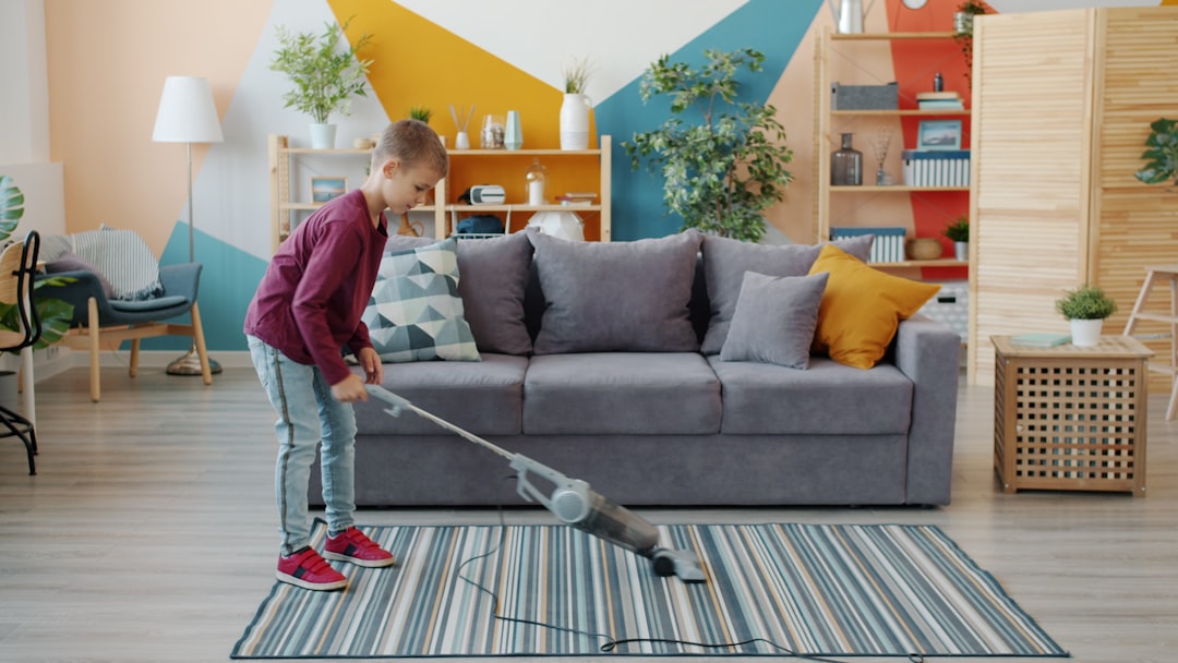 helpful little boy vacuuming floor at home using vacuum cleaner doing housework alone. Childhood, lifestyle and housekeeping concept.